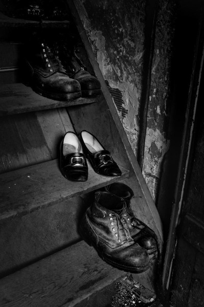 Wir sehen ein altes schwarz weiss Foto von drei Paar Schuhen auf einer Holztreppe:  zwei Paar Bergschuhe und ein Paat Trachtenschuhe einer Frau.
