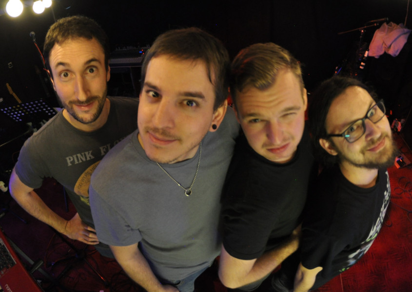 Die Bandmitglieder schauen nach oben in die Kamera. Es sind vier junge Männer. 