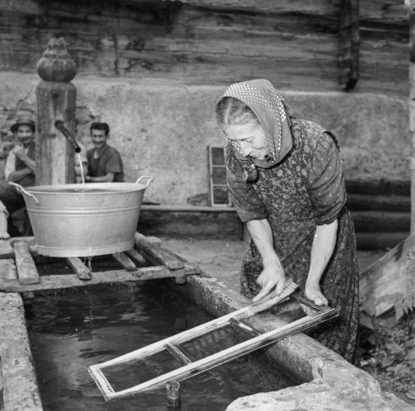 Luzia Agten-Imhof en train de nettoyer les vitres près de la fontaine du village (1953)