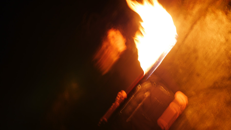 Man sieht eine verschwommene Flamme, dahinter Umrisse eines Menschen.