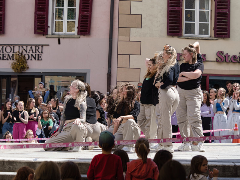 Auf dem Bild sieht man eine Tanzgruppe in beigen Hosen und schwarzen T-Shirts. Rund herum das Publikum auf dem Platz in Brig.