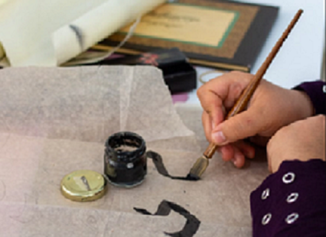 Enfant qui fait de la calligraphie avec un pinceau sur du papier, à côté d'un encrier