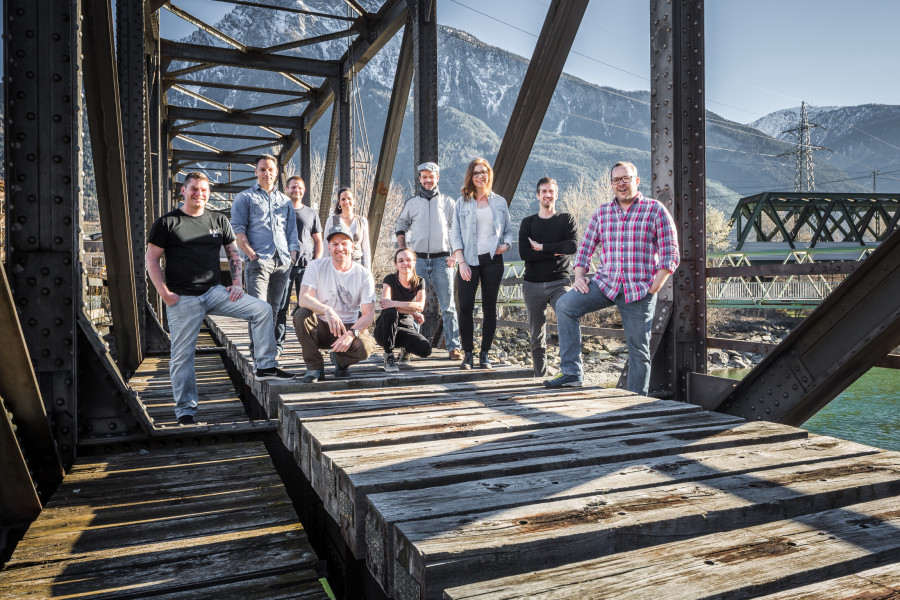 man sieht die 10 Musikerinnen und Musiker der Band auf einer alten Eisenbahnbrücke.