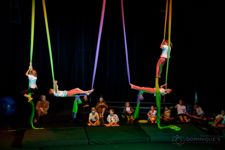 Zirkuskinder und ihre Eltern sitzen auf der Bühne. Vier Kinder klettern an bunten Tüchern.